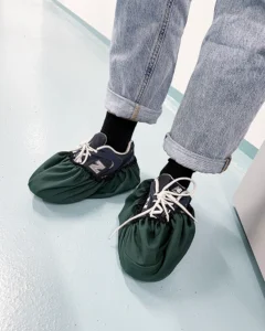 Genbrugsfutter i brug Person med jeans og sneakers iført mørkegrønne genbrugsfutter på et lyseblåt gulv.