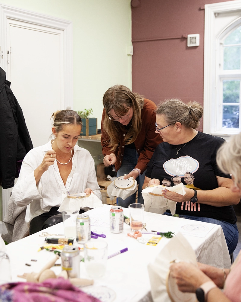 Fællesskab og kreativitet på vores visible mending workshop Gruppe af deltagere, der broderer synlige reparationer på en visible mending workshop.