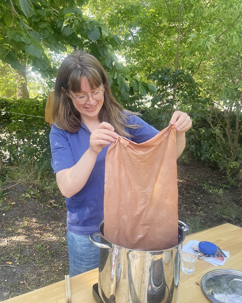 Lær plantefarvning – håndfarvning med naturlige ingredienser En person dypper et stykke stof i en gryde med plantefarve under en workshop.