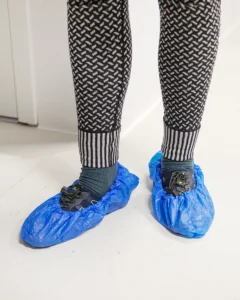 Engangsplastikfutter En person med strikkede leggings iført blå plastikfutter på et hvidt gulv.
