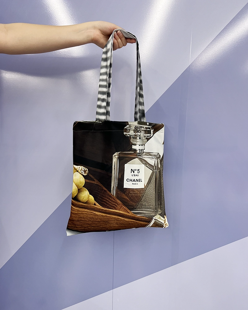Stofnet syet af et kasseret banner med et tryk af en Chanel-parfume, holdt af en person mod en lilla baggrund.