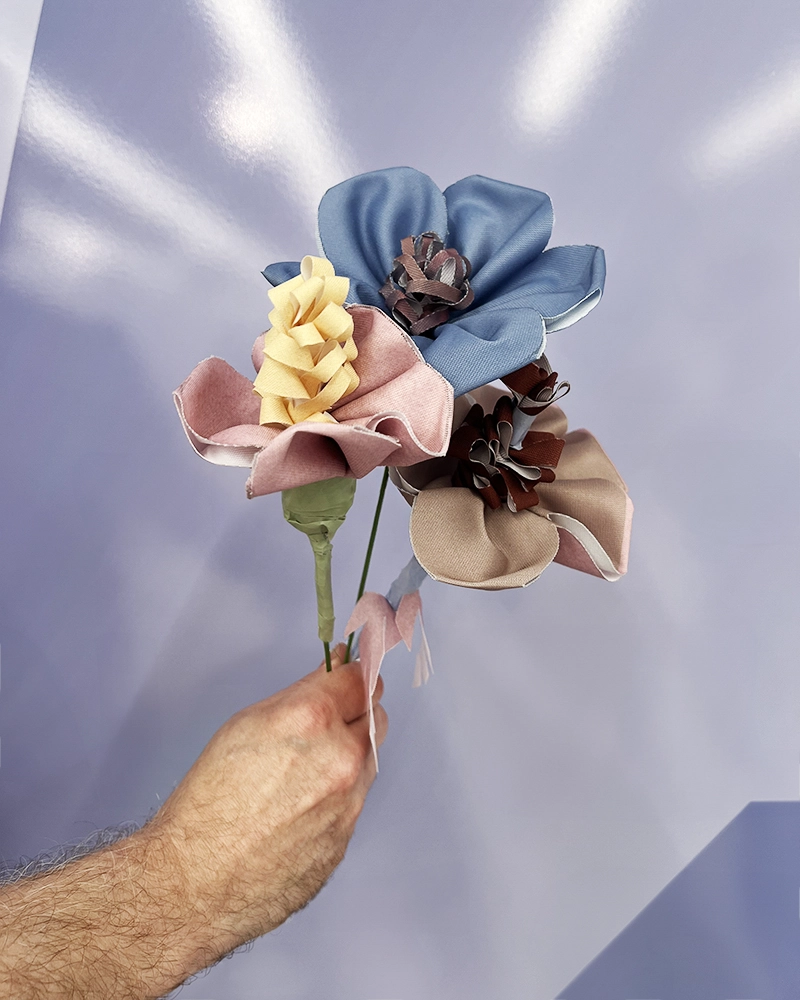 Hånd holder en buket af blomster lavet af genbrugsmaterialer.